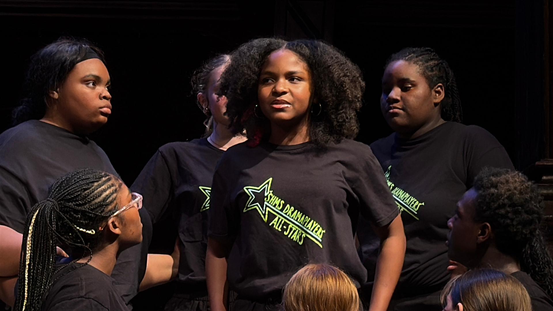Asherah Anu standing centre stage surrounded by her ensemble castmates