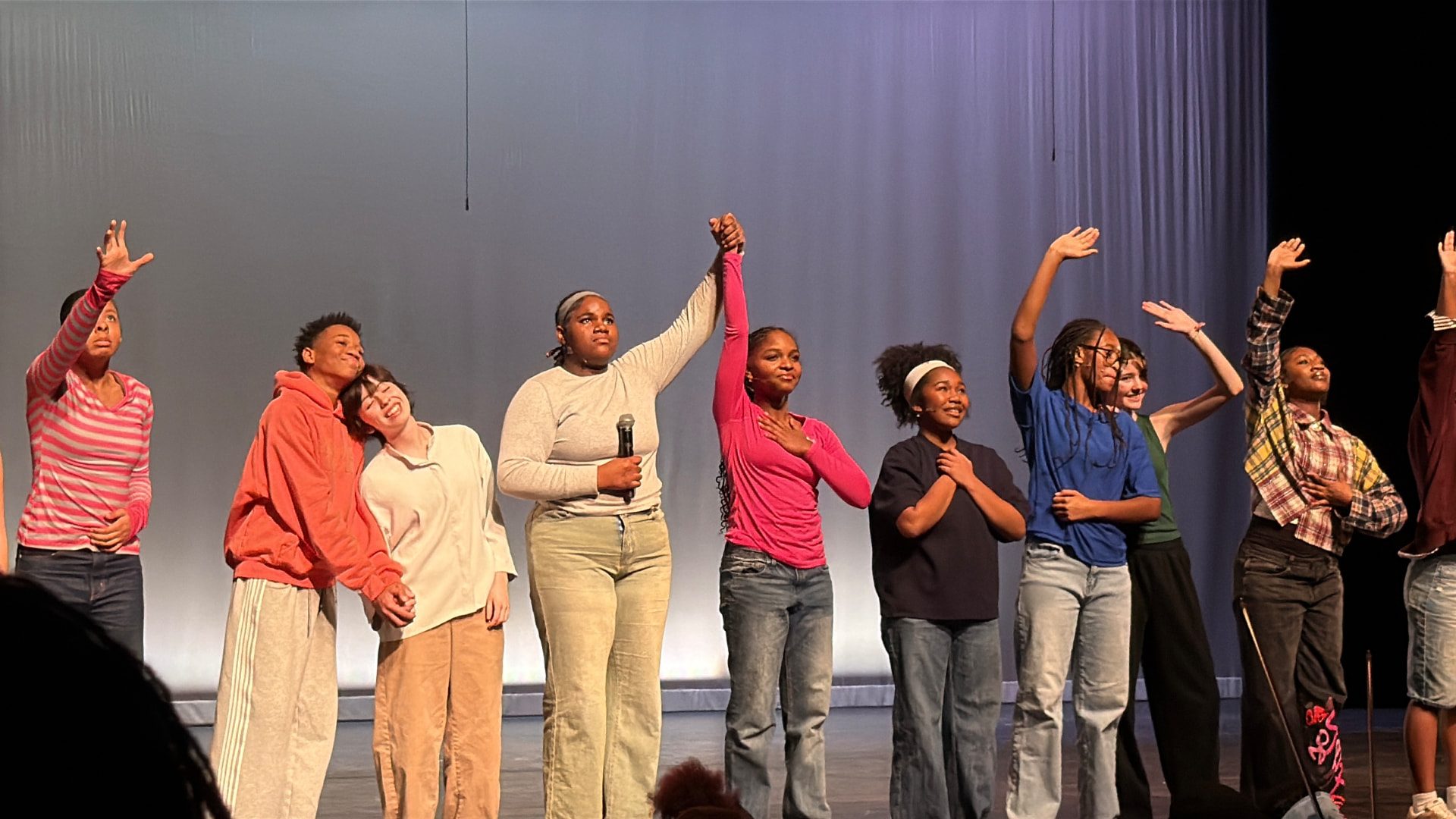 Asherah and her castmates taking a bow with arms raised on stage