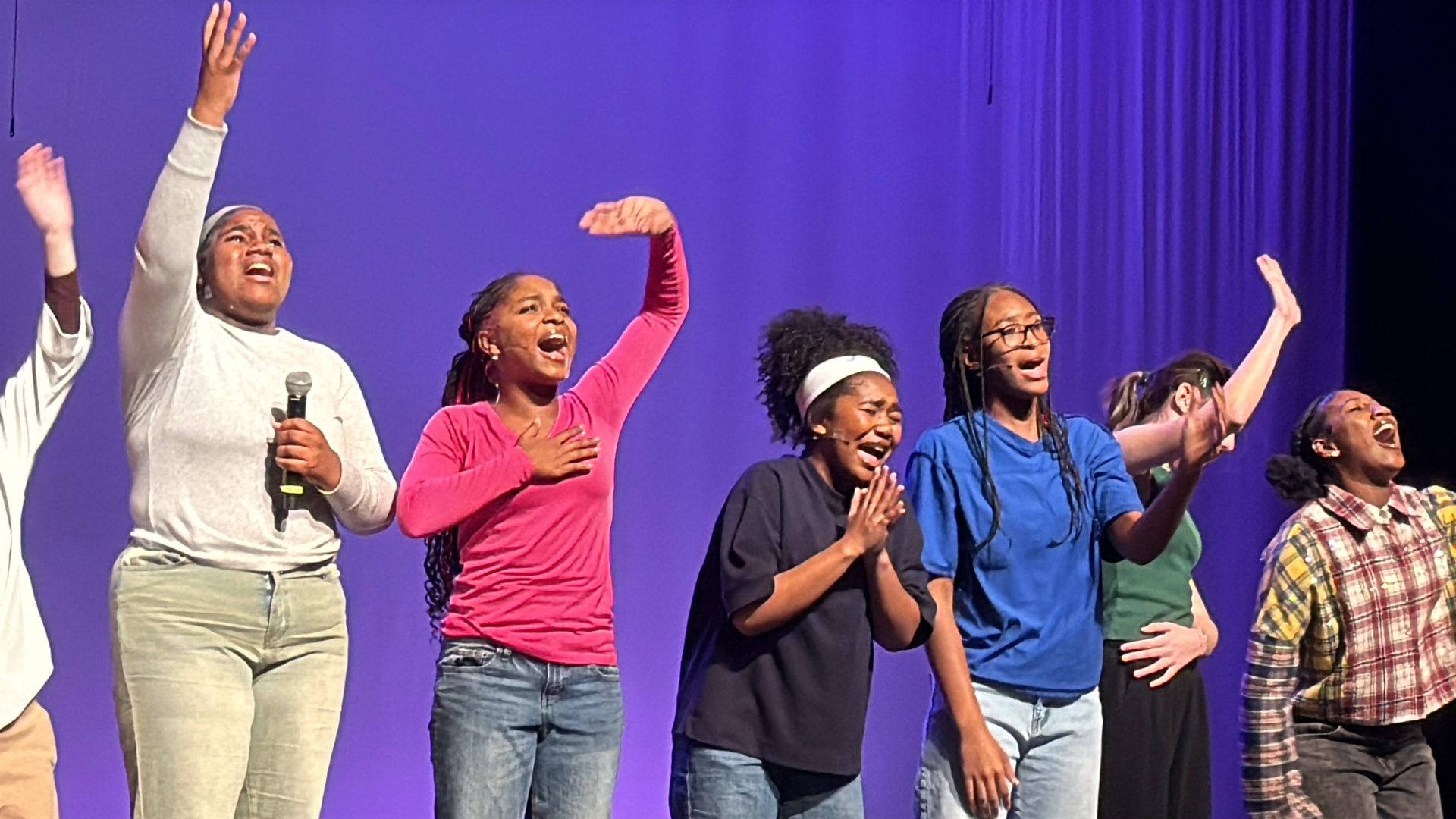 Asherah singing with her ensemble under purple stage light